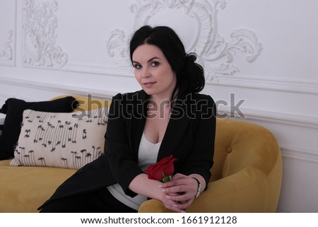  woman of thirty in a good mood in a trouser suit sits on a yellow sofa