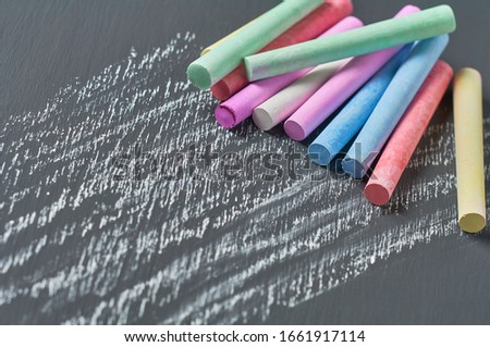 Heap of many colorful pieces of chalk on black chalkboard. Close-up