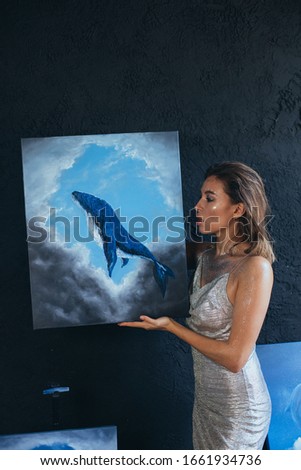 Beautiful woman artist with creative fantasy make up posing with her paintings.