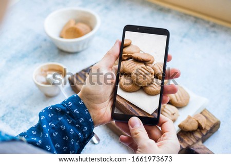 Woman make picture of homemade peanut butter cookies at kitchen or cafe with phone or smartphone. Food photography for social media and networks style or blogging. Vegan and vegetarian healthy food.