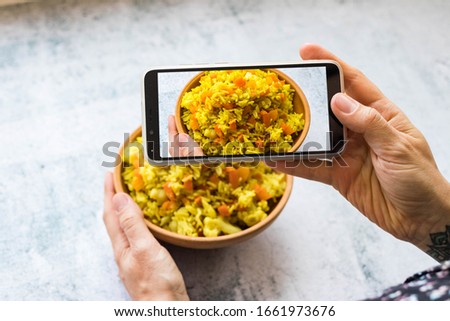 Woman make picture of basmati Indian vegetables rice at kitchen or cafe with phone or smartphone. Food photography for social media and networks style or blogging. Vegan and vegetarian healthy food.