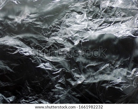 Background cellophane texture on a black background. Abstract background of a plastic bag. Crumpled plastic bag close-up. The pattern and the background. Copy space.