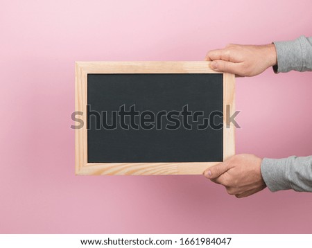 Men's hands hold a black board, an empty blank, a frame, on a pink background. Copy space.