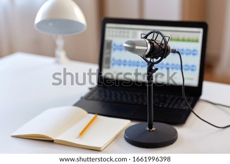 post production and technology concept - microphone, laptop computer with sound editor program, headphones and notebook on table at home office