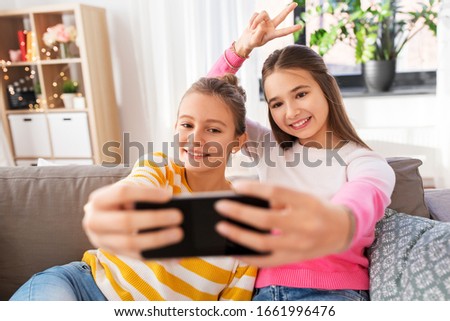 people, technology and friendship concept - happy teenage girls taking selfie with smartphone sitting on sofa at home