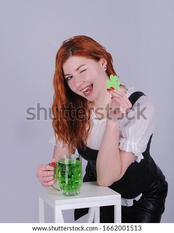 Beautiful woman in dress with glass of green beer and paper clover is posing on grey background. Happy St. Patrick's Day.