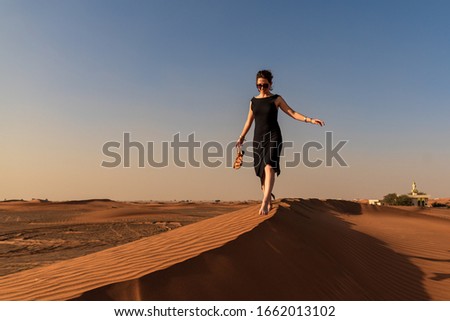 Woman walks down the red dune before sunset in a black dress 
