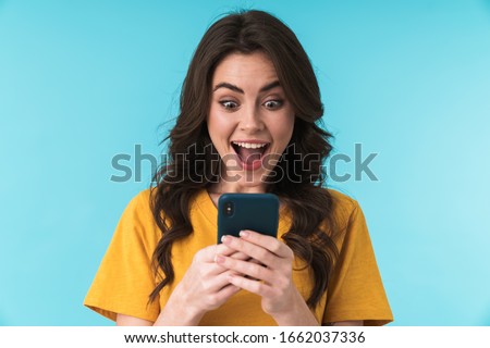 Image of a happy surprised shocked young pretty woman posing isolated over blue wall background using mobile phone.