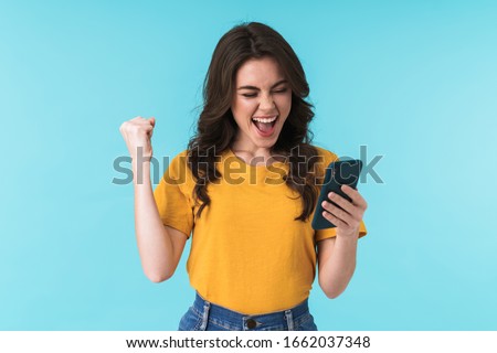 Image of a happy surprised young girl isolated over blue wall background using mobile phone make winner gesture. Royalty-Free Stock Photo #1662037348