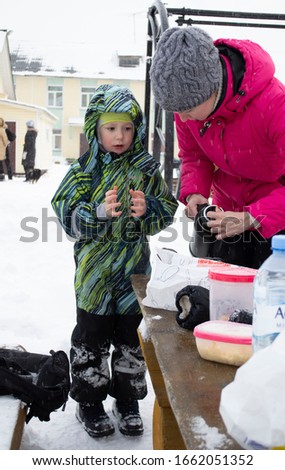 Mom pours hot tea to the boy in the winter on a picnic. rest at the winter base. russia arkhangels region