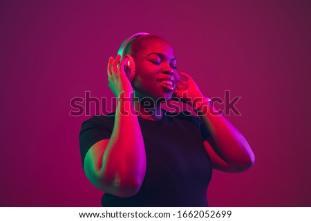Listen to music. African-american young woman's portrait on purple background. Beautiful model in wireless headphones. Concept of emotions, facial expression, sales, ad, inclusion. Copyspace.