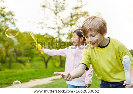 Two children are making soap bubbles together in the park in kindergarten or preschool