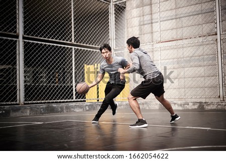 two young asian adult men playing one-on-one basketball on outdoor court