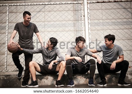 group of four asian young adult men resting relaxing talking chatting on outdoor basketball court