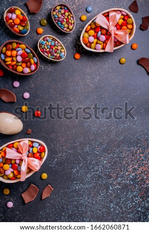 Chocolate Easter border with chocolate eggs and colorful candy sweets on dark concrete black background, copy space. Traditional Easter treats flat lay, holiday background