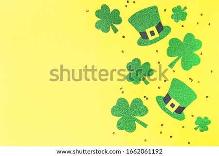 Saint Patrick's day holiday card with green shamrock symbols, hat, golden confetti. Traditional St. Patrick's Day green attire and decorations on yellow background.