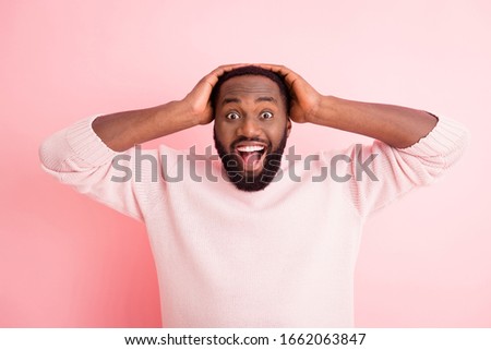 Photo of funny attractive dark skin young guy toothy beaming smiling listen good news open mouth arms on head wear warm knitted sweater isolated pink color background