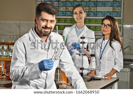A team of scientists works in the laboratory. Man and woman in white bathrobes on background of periodic system of elements. Scientists conduct experiments in chemistry.