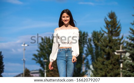 Portrait of young beautiful brunette woman in jeans and white blouse walking in summer street