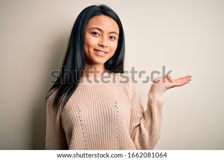 Young beautiful chinese woman wearing casual sweater over isolated white background smiling cheerful presenting and pointing with palm of hand looking at the camera.