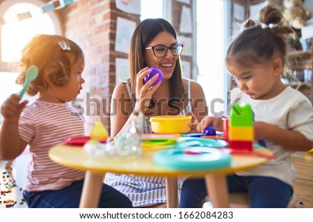 Young beautiful teacher and toddlers playing meals using plastic food and cutlery toy at kindergarten Royalty-Free Stock Photo #1662084283
