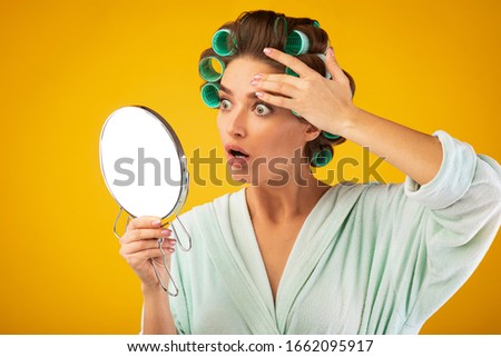 Glamorous Housewife Stressing About Wrinkles Touching Face Looking In Mirror Standing On Yellow Studio Background. Fear Of Aging Concept