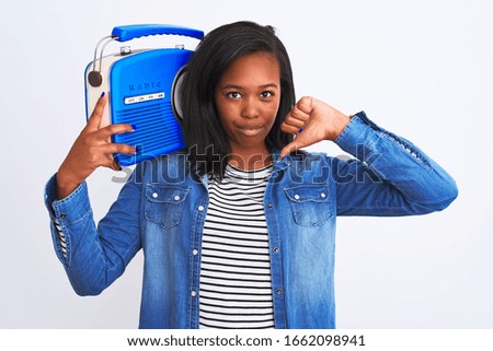 Young african american woman holding vintage retro radio over isolated background with angry face, negative sign showing dislike with thumbs down, rejection concept