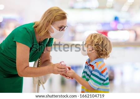 Family with kids in face mask in shopping mall or airport. Mother and child wear facemask during coronavirus and flu outbreak. Virus and illness protection, hand sanitizer in public crowded place. Royalty-Free Stock Photo #1662104719