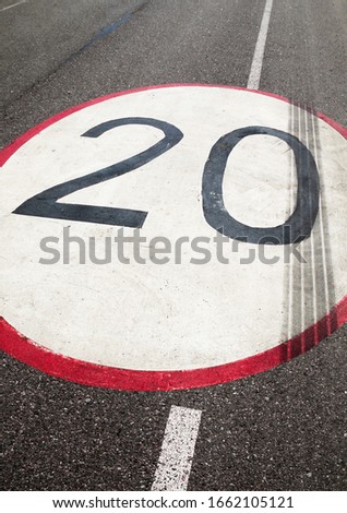 Speed limit sign (20 kilometers/miles per hour) painted on the asphalt surface. 