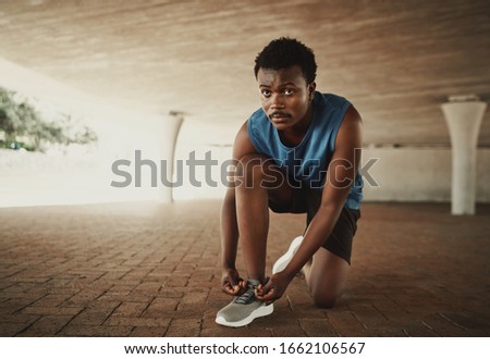 Portrait of a confident male jogger tying his shoelaces on pavement under the bridge
