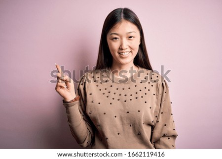 Young beautiful asian woman wearing fashion and elegant sweater over pink solated background with a big smile on face, pointing with hand finger to the side looking at the camera.