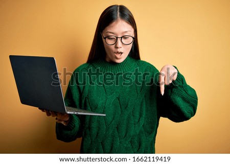 Young asian business woman wearing glasses and working using computer laptop Pointing down with fingers showing advertisement, surprised face and open mouth
