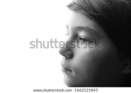 Black and white portrait of young sad boy crying with sad eyes. White background. Free space for text. Tear on cheek of unhappy teenager.