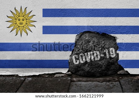 Flag of Uruguay on the wall with cracked stone with Coronavirus name on it. 2019 - 2020 Novel Coronavirus (2019-nCoV) concept, for an outbreak occurs in the Oriental Republic of Uruguay.