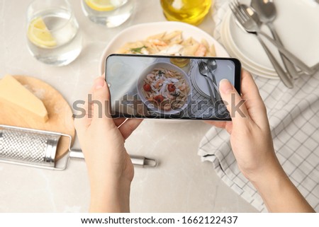 Food blogger taking picture of tasty pasta with shrimps and tomatoes at light table, closeup
