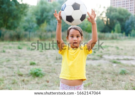 Outdoor photo of cute little girl leaning on soccer ball in green grass