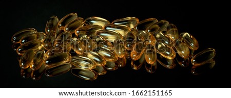 Many fish oil capsules on a black mirror surface with reflections isolated on black background.