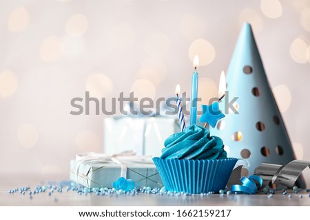 Delicious birthday cupcake with cream and burning candles on white table. Space for text
