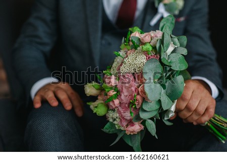 groom holds in his hands a bridal bouquet of natural flowers