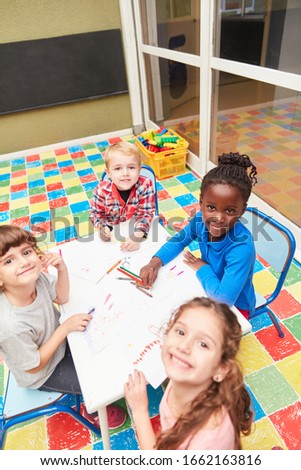 Group of happy kids while painting in kindergarten at the table with crayons