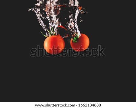 Closeup of fresh and health cherry tomatoes falling into clear water with big splash on black background. Group of fresh tomatoes falling into water with splash. Red tomato drop in water with bubble