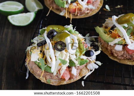 Chicken tostadas with jalapeno peppers, black olives, sour cream, lettuce, shredded chicken, fresh cilantro, onions, diced tomatoes, refried beans, avocados, and fresh limes.