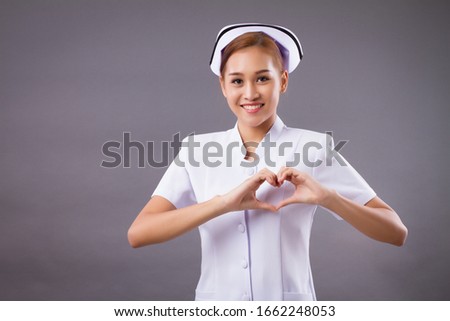 portrait of smiling asian woman nurse with heart hand sign isolated; friendly professional female nurse or medical worker with heart gesture for heart care service or body care or health care concept