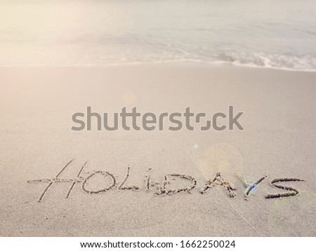 Holidays handwritten on sandy beach with soft wave and sun with copy space. Summer holiday. Sea, beach and relax.