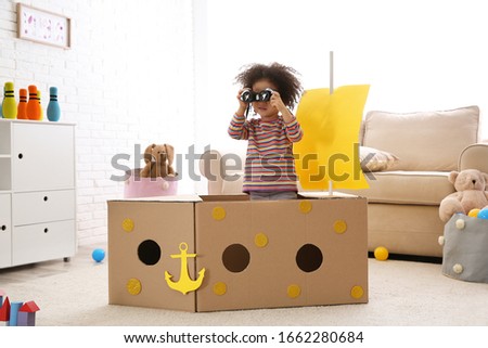 Cute African American child playing with cardboard ship and binoculars at home Royalty-Free Stock Photo #1662280684