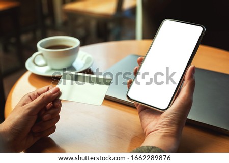 Mockup image of a hands holding credit card and a mobile phone with blank desktop screen in office