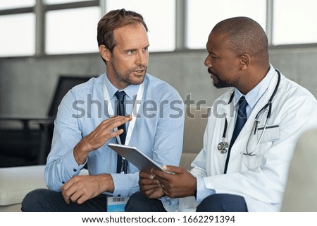 Pharmaceutical representative talking with doctor. African mature practitioner discussing results of the analysis with specialist while consulting diagnosis on digital tablet in hospital room. Royalty-Free Stock Photo #1662291394