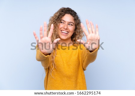 Young blonde woman with curly hair isolated on blue background counting ten with fingers