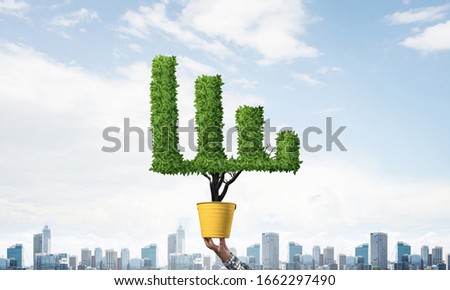 Green plant in shape of growth financial graph in yellow pot. Business analytics and statistics. Friendly ecosystem for business and investment. Human hand holding pot with green plant.