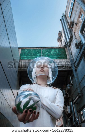 Albino girl in a spacesuit holds a plant
